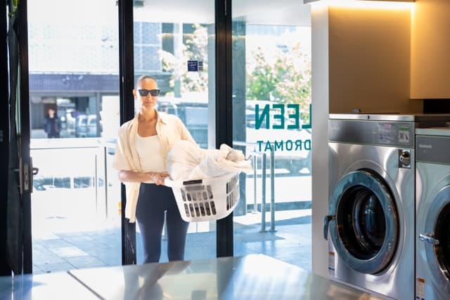 Customer arriving at the Spakleen St Kilda laundromat carrying a full laundry basket through the door