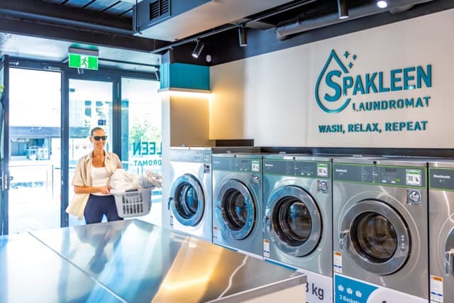 Customer walking into the Spakleen St Kilda laundromat with a laundry basket past a row of washing machines