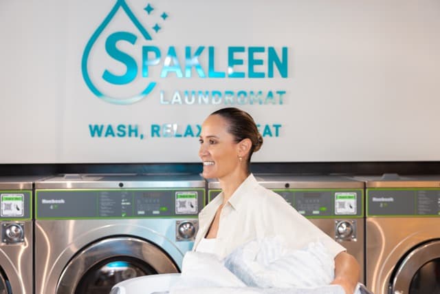Customer at Spakleen St Kilda with a basket of freshly washed laundry beside the machines