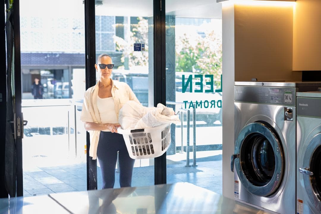 Customer carrying a full laundry basket through the door of a Spakleen laundromat