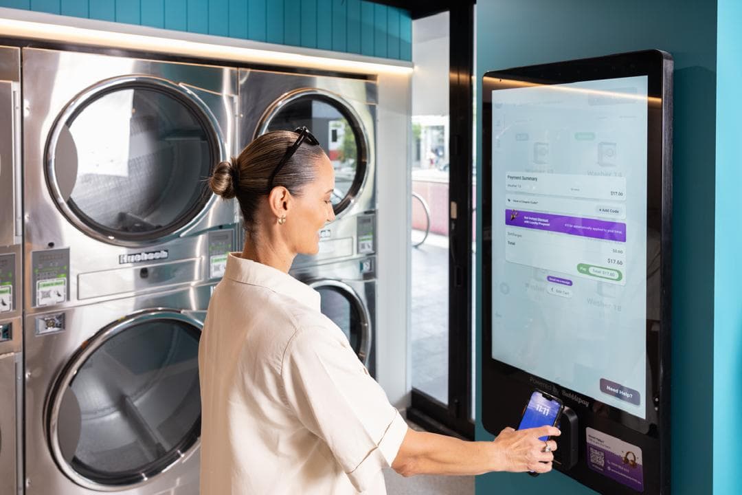 Customer paying at the Spakleen cashless payment kiosk with a phone, next to stacked dryers